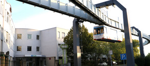 Foto von dem weißen CDI-Gebäude bei Sonnenuntergang mit vorbeifahrender Schwebebahn der TU Dortmund.